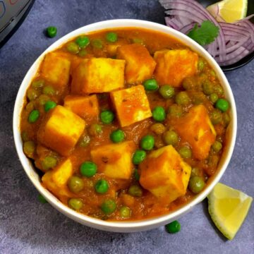 matar paneer served in a white bowl with lemon wedges and onion on the side