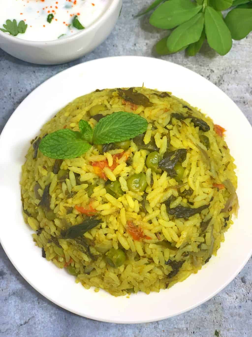 methi rice bath served in a plate garnished with mint leaves with side of raita