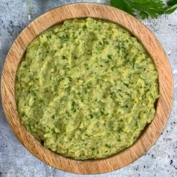 green tomato chutney served in a wooden bowl with cilantro and raw tomato on the side