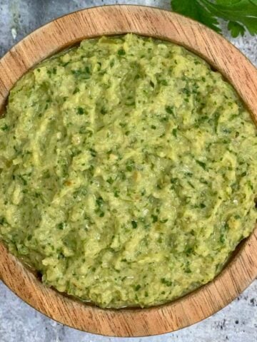 green tomato chutney served in a wooden bowl with cilantro and raw tomato on the side