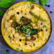 millet pongal served in a bowl with tempering on top and black pepper on side