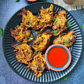 air fried onion pakoda served on a plate with ketchup and green chutney on the side with tea