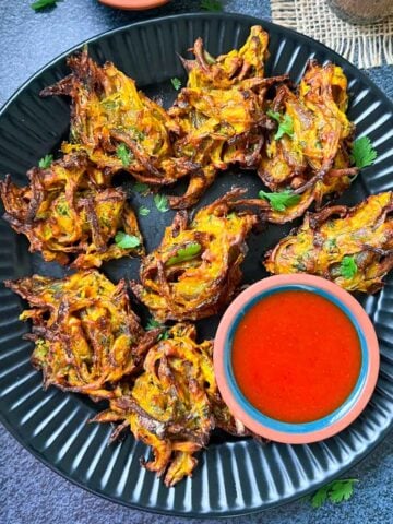 air fried onion pakoda served on a plate with ketchup and green chutney on the side with tea