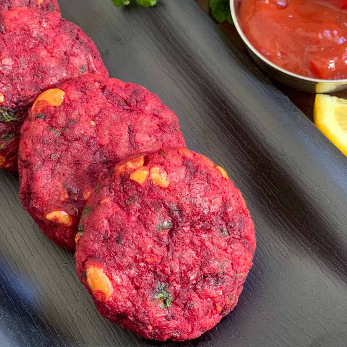 beetroot cutlets arranged in a row on a black plate with ketchup on the side