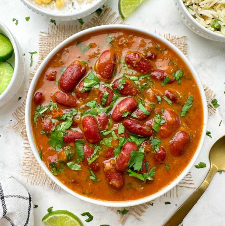 instant pot rajma masala curry (indian kidney beans curry) served in a bowl garnished with coriander leaves with boondi raita and jeera rice on the side with a lime wedge
