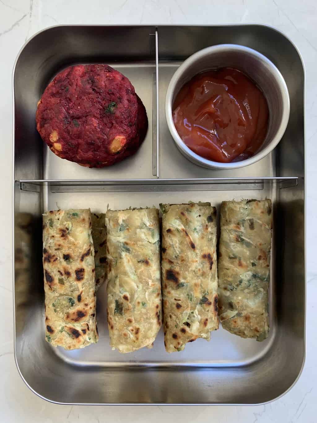 Lauki Paratha, beetroot tikki, and tomato Ketchup  in bento steel lunch box.