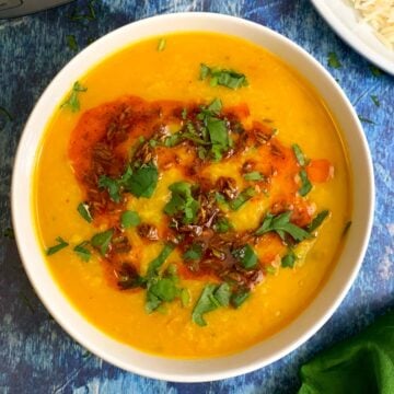 Moong Dal Tadka served in a white bowl with tempering on top garnished with cilantro