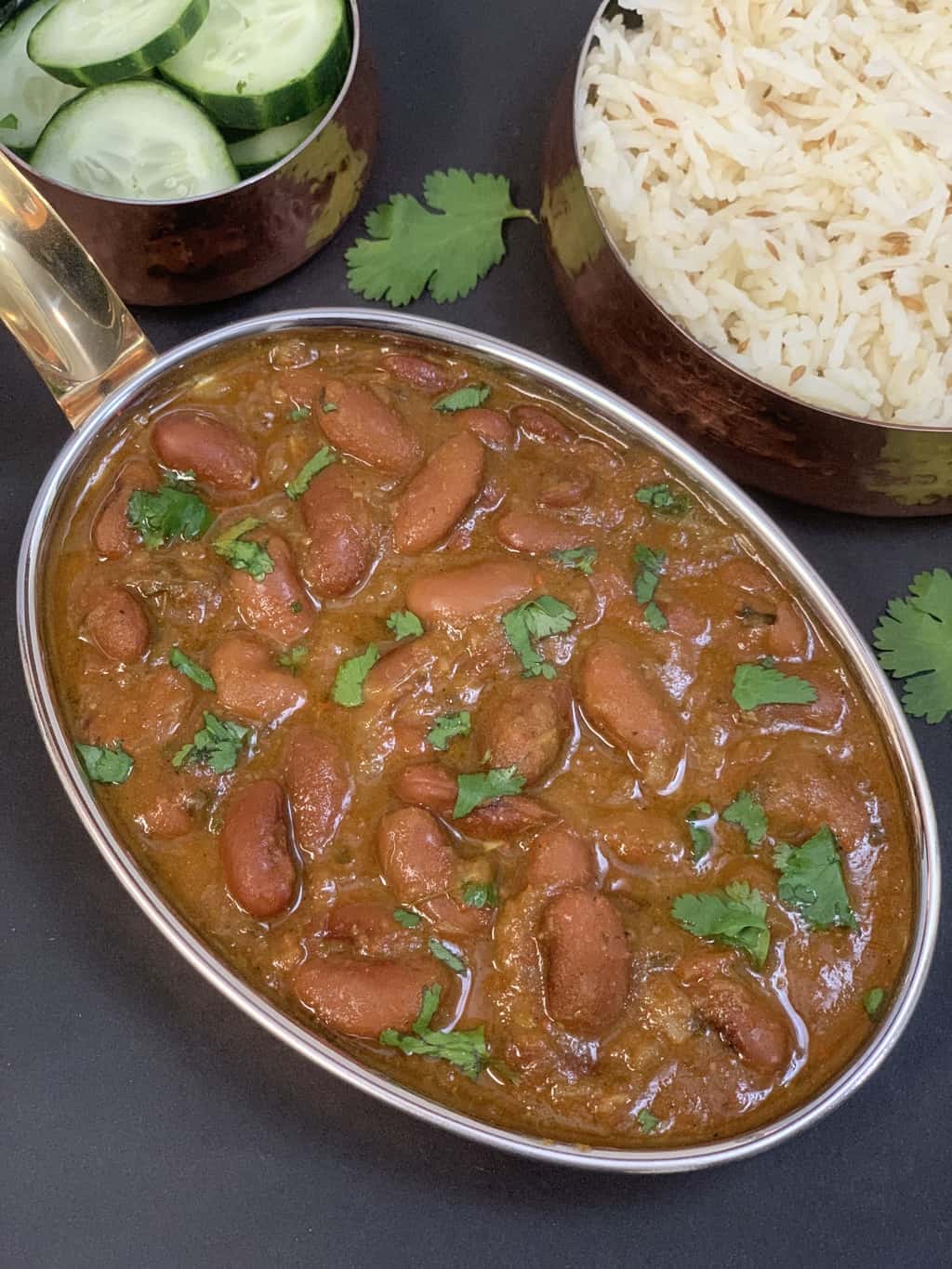 rajma masala served in a kadai with side of rice and cucumber