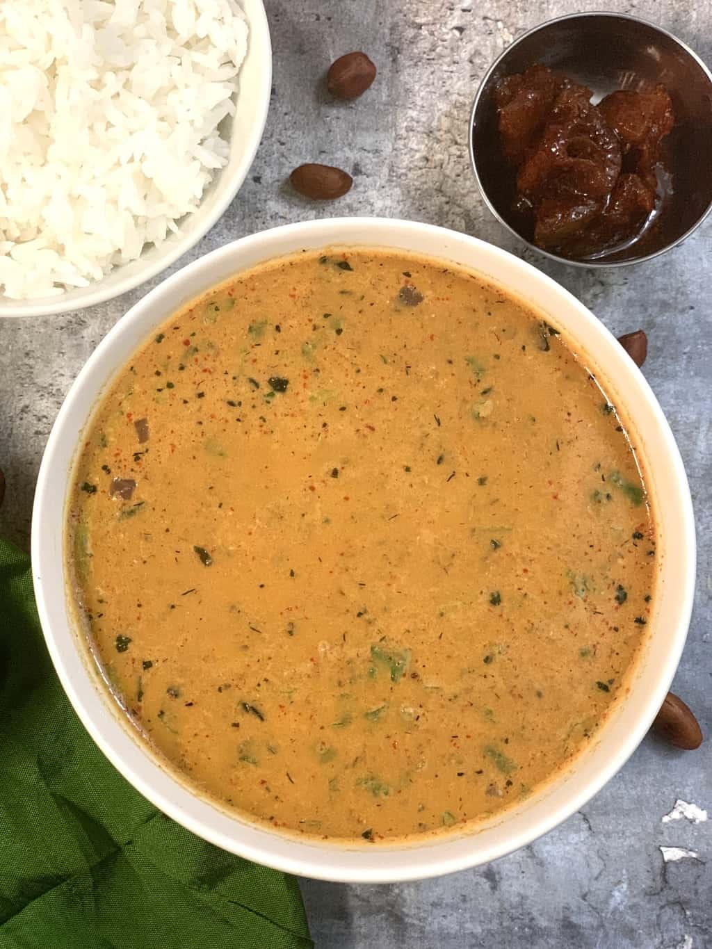 peanut sambar/shenga saaru served in a white bowl with side of pickle and white rice