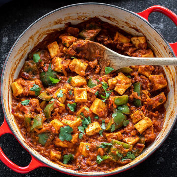 Kadai paneer in a dutch oven with a wooden spoon in it.