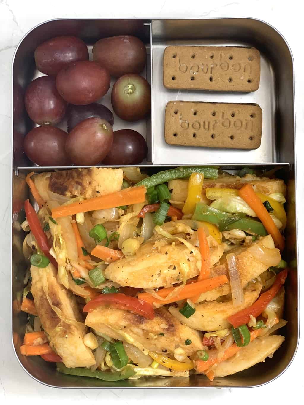 Vegetable Fried Idli, Bourbon Biscuit and Grapes in steel bento lunch box.