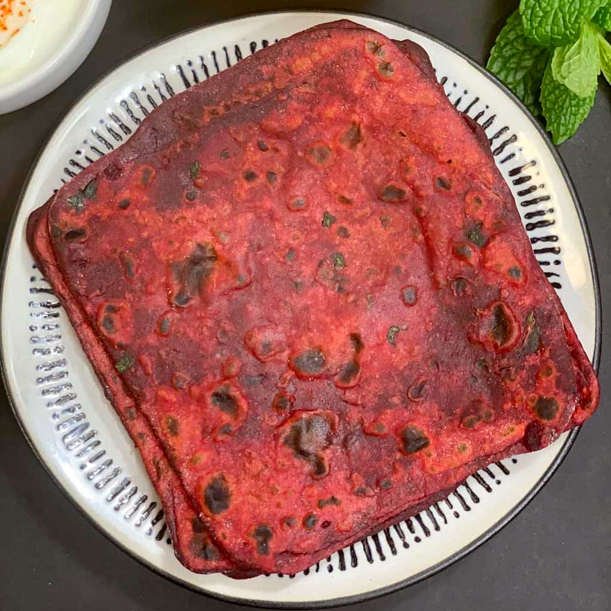 square Beetroot Parathaserved on a plate with raita on side