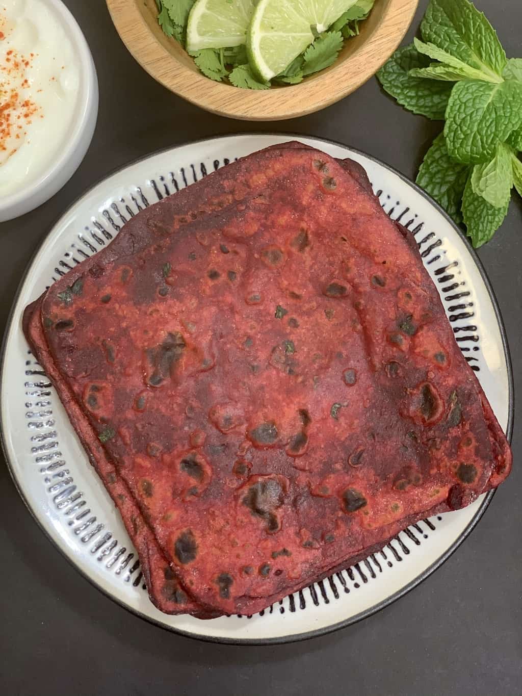 beetroot paratha served on a white plate with raita and lemon wedges on the side