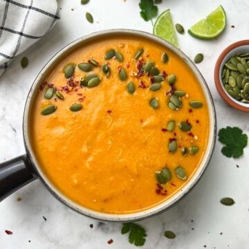 butternut squash soup served in a bowl with pumpkin seeds and red chili flakes on the top