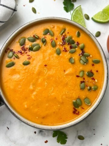 butternut squash soup served in a bowl with pumpkin seeds and red chili flakes on the top