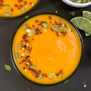 Butternut Squash Soup served in a black bowl garnished with red chilli flakes and pumpkin seeds