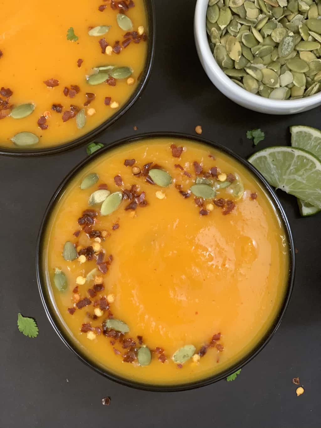 butternut squash soup served in a bowl garnished with red chilli flakes and pumpkin seeds