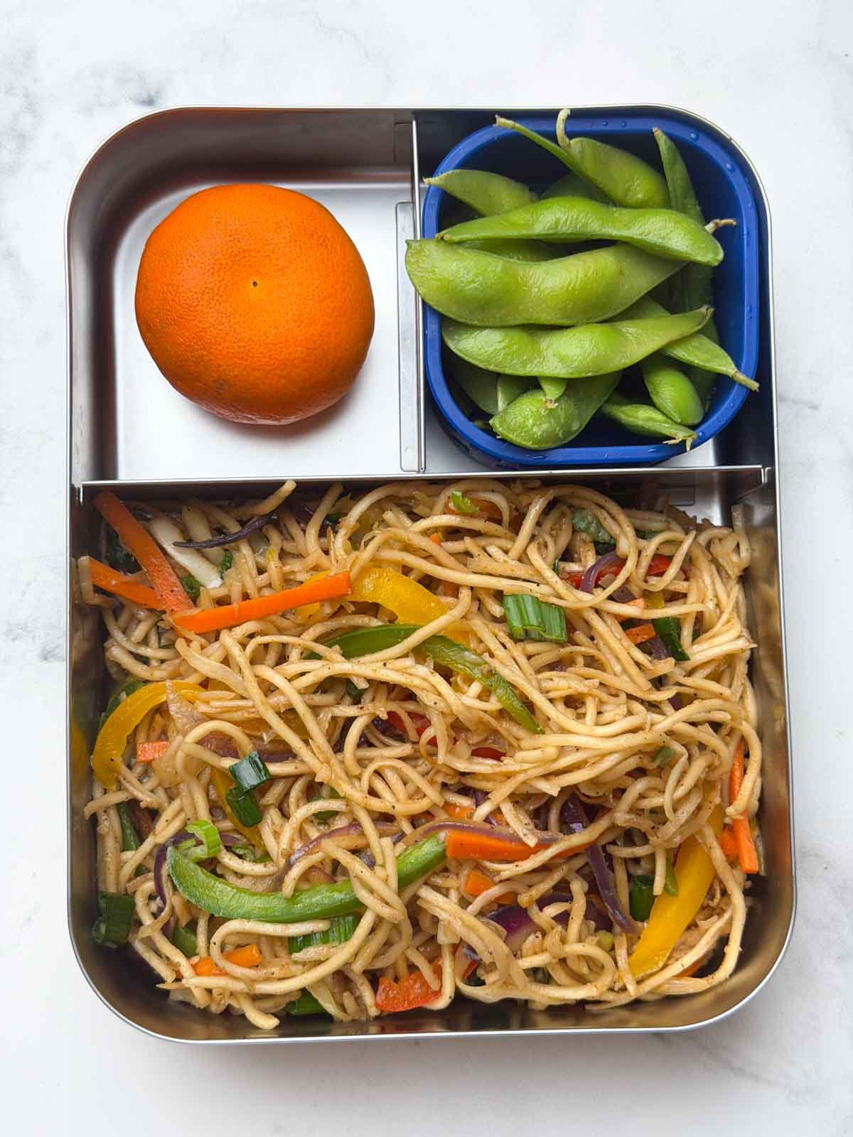 Kids bento lunch box with veg hakka noodles, steamed edamame and orange