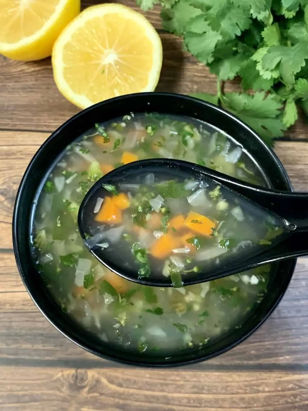 Lemon Coriander Soup served ina black soup bowl and lemon wedges and cilantro on the side
