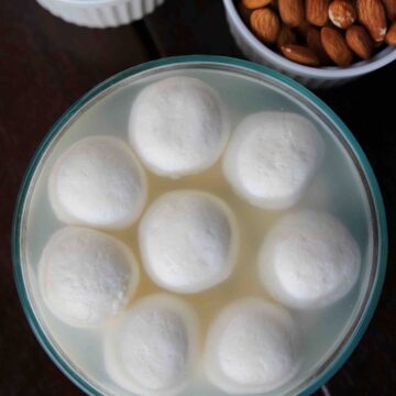 rasgulla served in a glass bowl with whole almonds and boondi on the side.