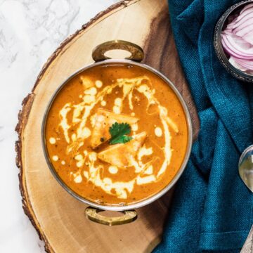 shahi paneer served in a kadai with raw onions on the side.