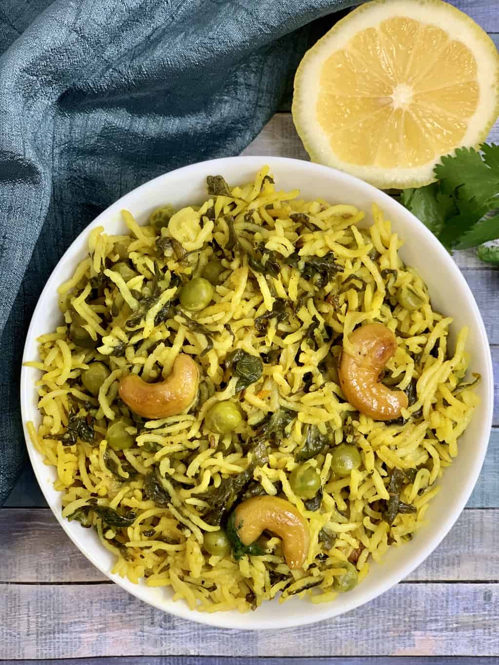 spinach rice served in a white bowl garnished with cashew-nuts with lemon on the side