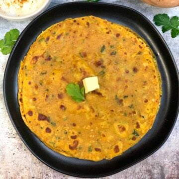 Sweet Potato Paratha served on a plate topped with butter and raita on the side