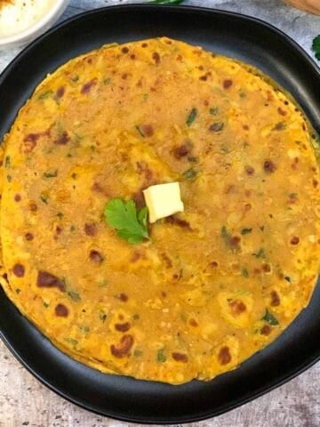 Sweet Potato Paratha served on a plate topped with butter and raita on the side