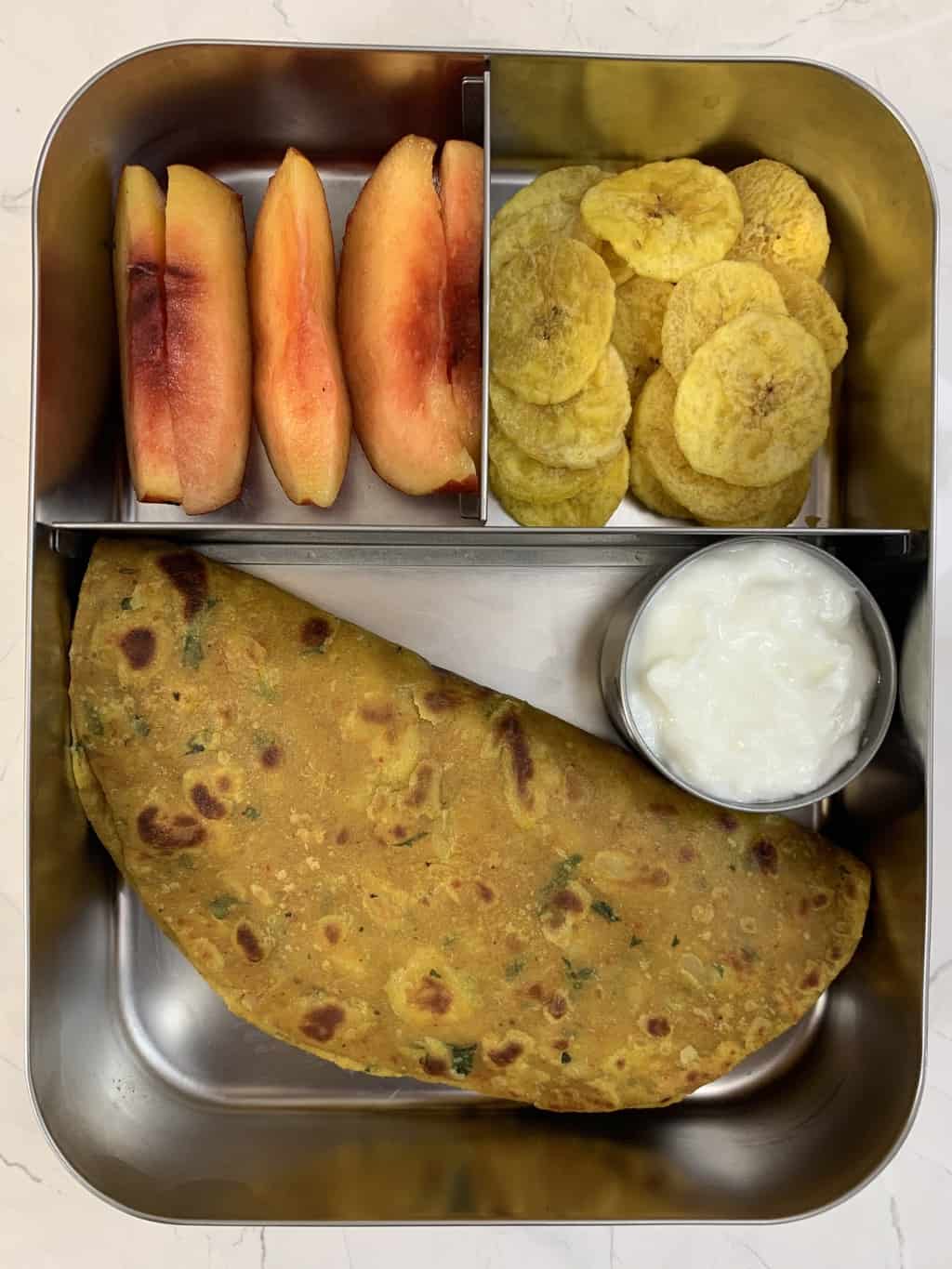 sweet potato parathas with yogurt, banana chips, and peach in steel bento box.