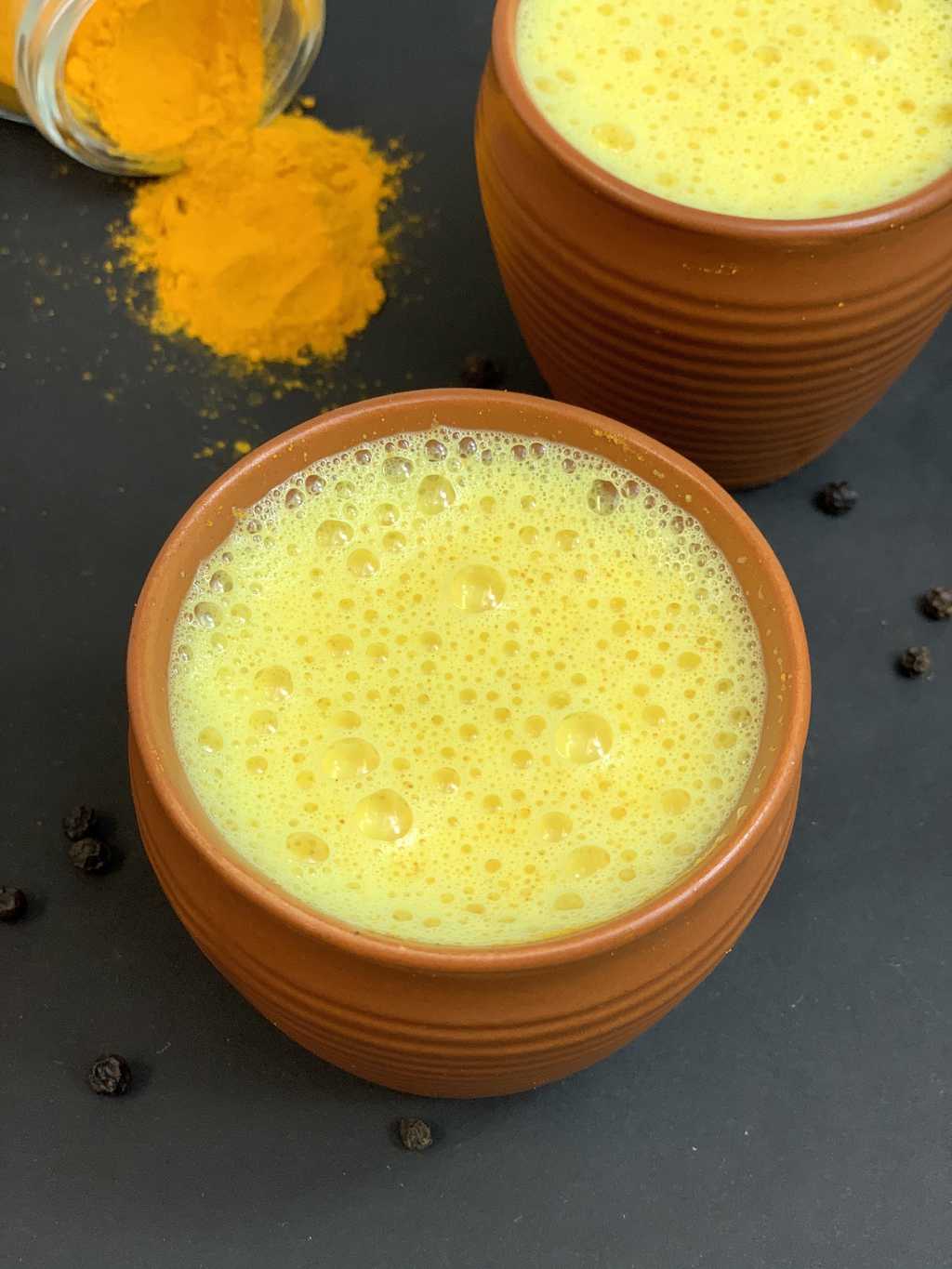 golden turmeric milk served in a mud pot with turmeric on the side