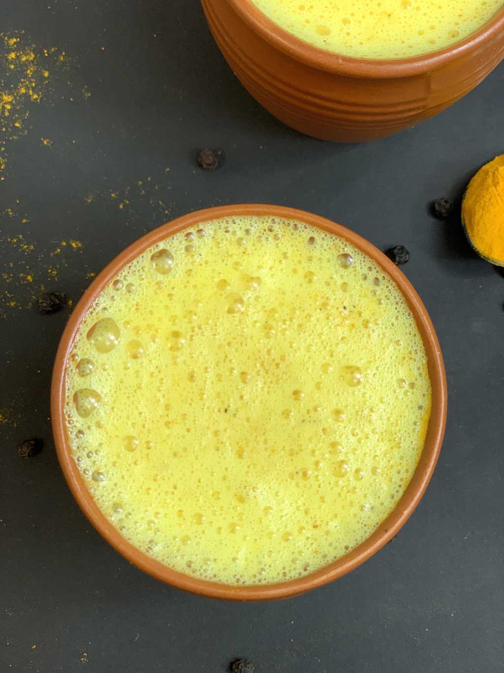 golden milk served in a serving mud pot with turmeric powder and black pepper on the side