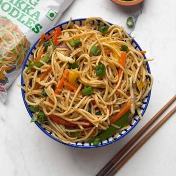 Vegetable hakka noodles served in a bowl, with side of chopped green spring onions, chings hakka noodles packet and chop sticks