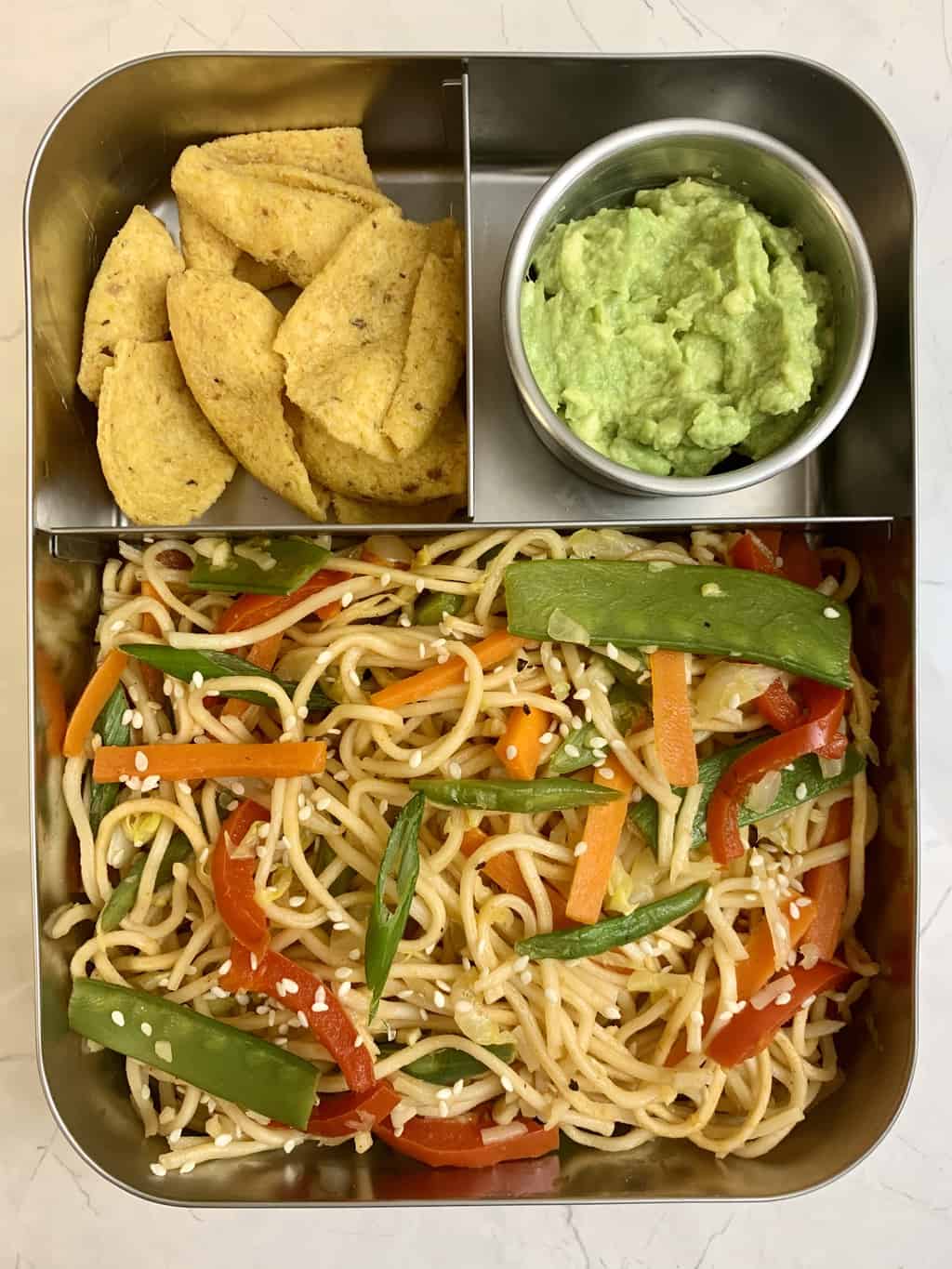 Veg Chow Mein, Guacamole, Corn Chips in steel bento lunch box.