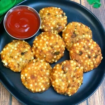 7 pieces of sabudana vada served on a plate with a small bowl of tomato ketchup on side