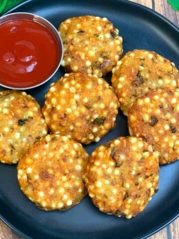 7 pieces of sabudana vada served on a plate with a small bowl of tomato ketchup on side