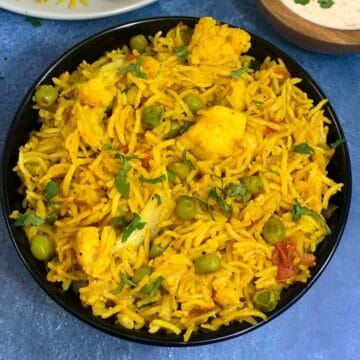 cauliflower pulao served in a bowl with raita on the side