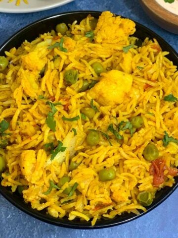 cauliflower pulao served in a bowl with raita on the side