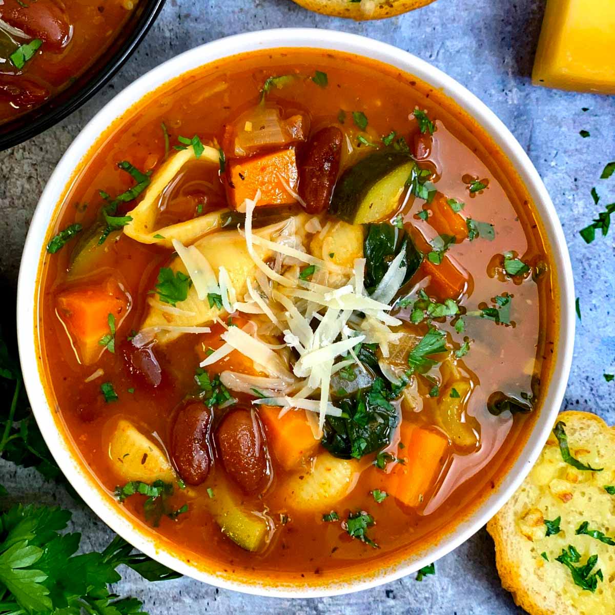 olive garden minestrone soup served in a white bowl with parmesan cheese on top and garlic bread ,parsley on side