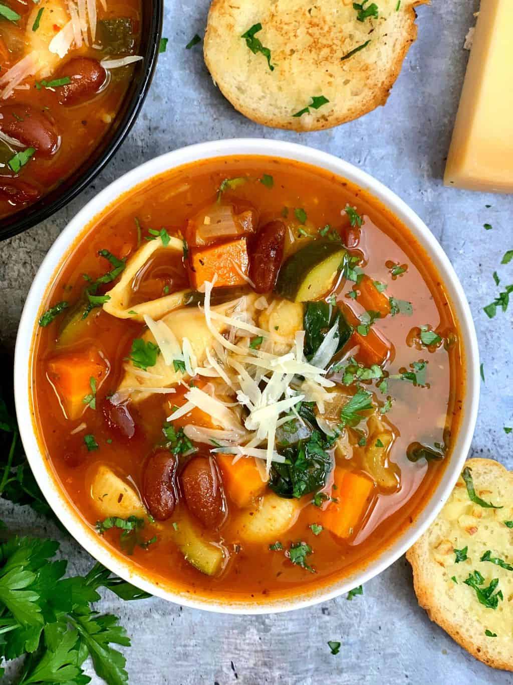 minestrone soup served in a soup bowl garnished with cheese and parsley with garlic bread on the side