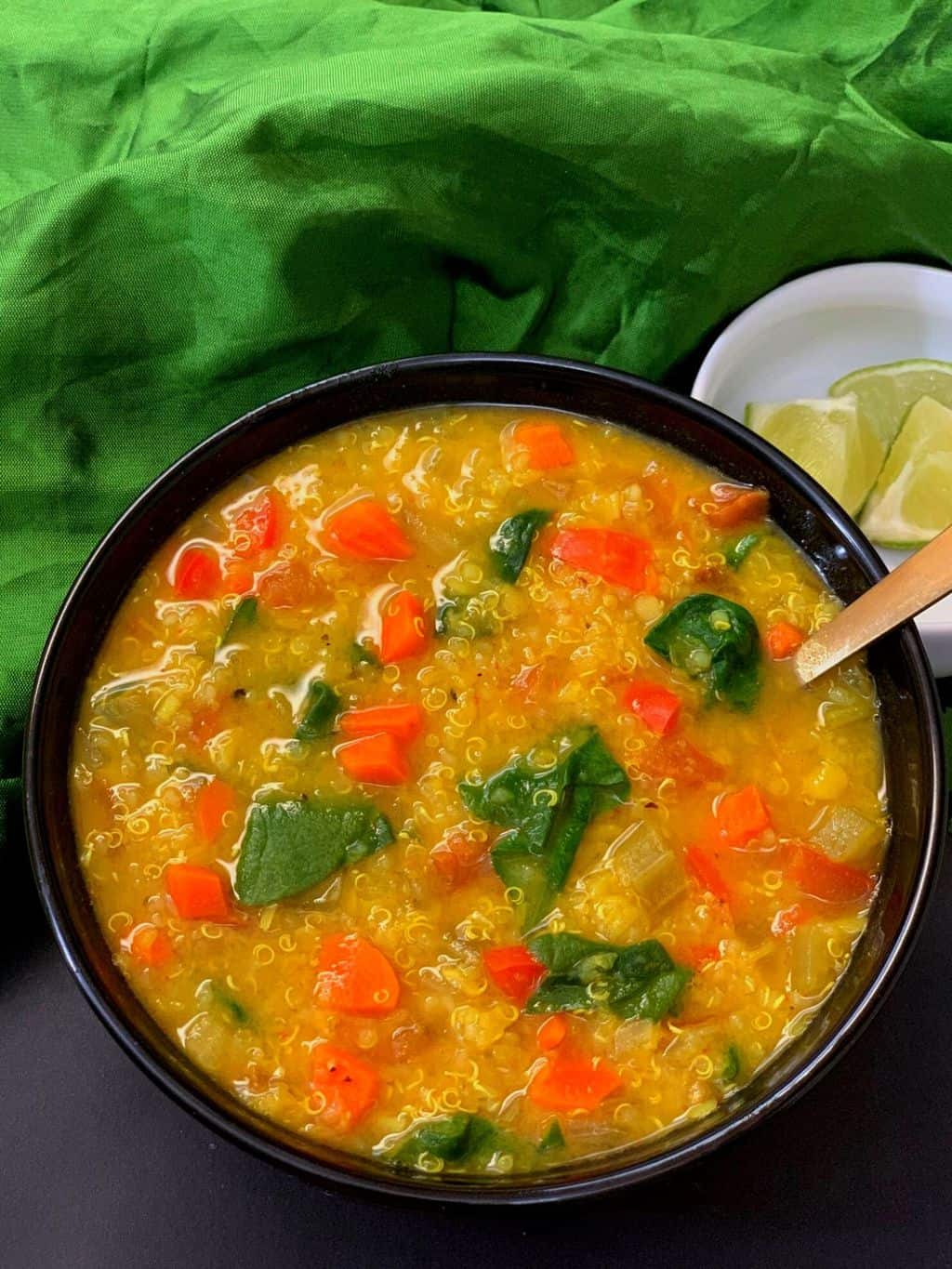 vegetable quinoa lentil soup served in a bowl with a spoon and lemon wedges on the side