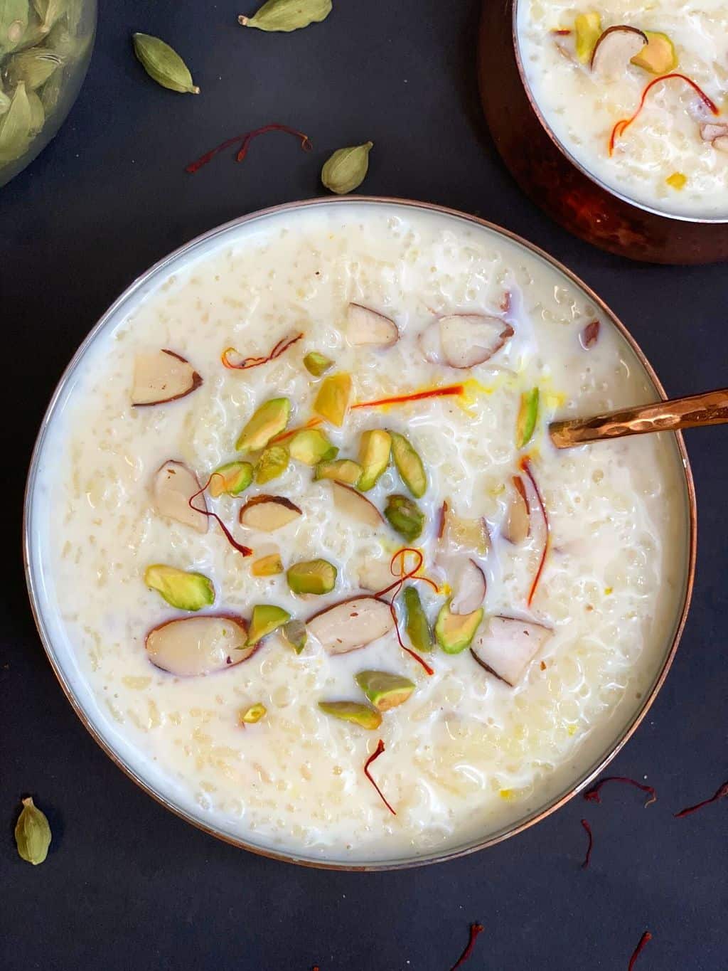Instant Pot Rice Kheer recipe served in a bowl garnished with nuts with a spoon on top and cardamom on the side