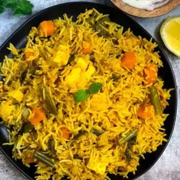 instant pot vegetable biryani served in a black plate with raita and lemon wedges on the side