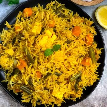 instant pot vegetable biryani served in a black plate with raita and lemon wedges on the side