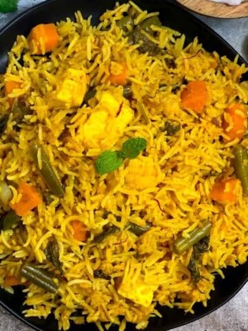 instant pot vegetable biryani served in a black plate with raita and lemon wedges on the side