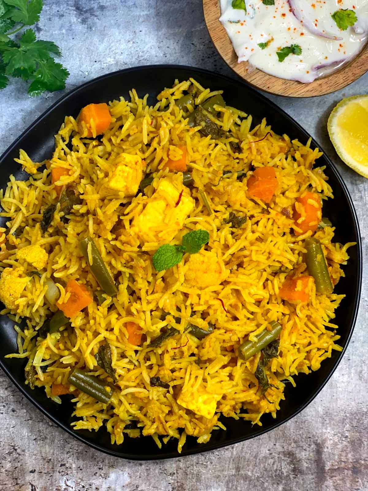 instant pot vegetable biryani served in a black plate with raita and lemon wedges on the side