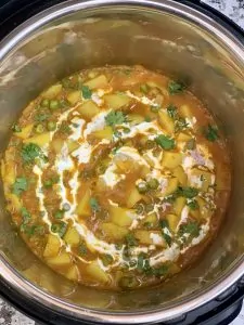 aloo matar in the instant pot insert garnished with cashew cream and cilantro
