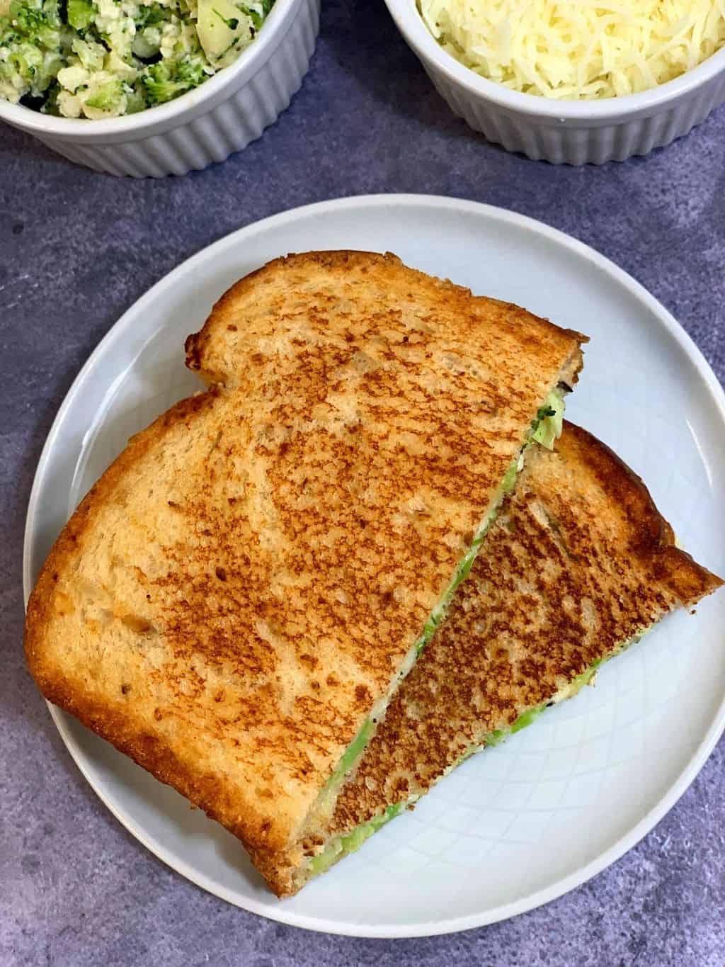 Broccoli Paneer Mayo Sandwich cut into half served on a plate with cheese on the side