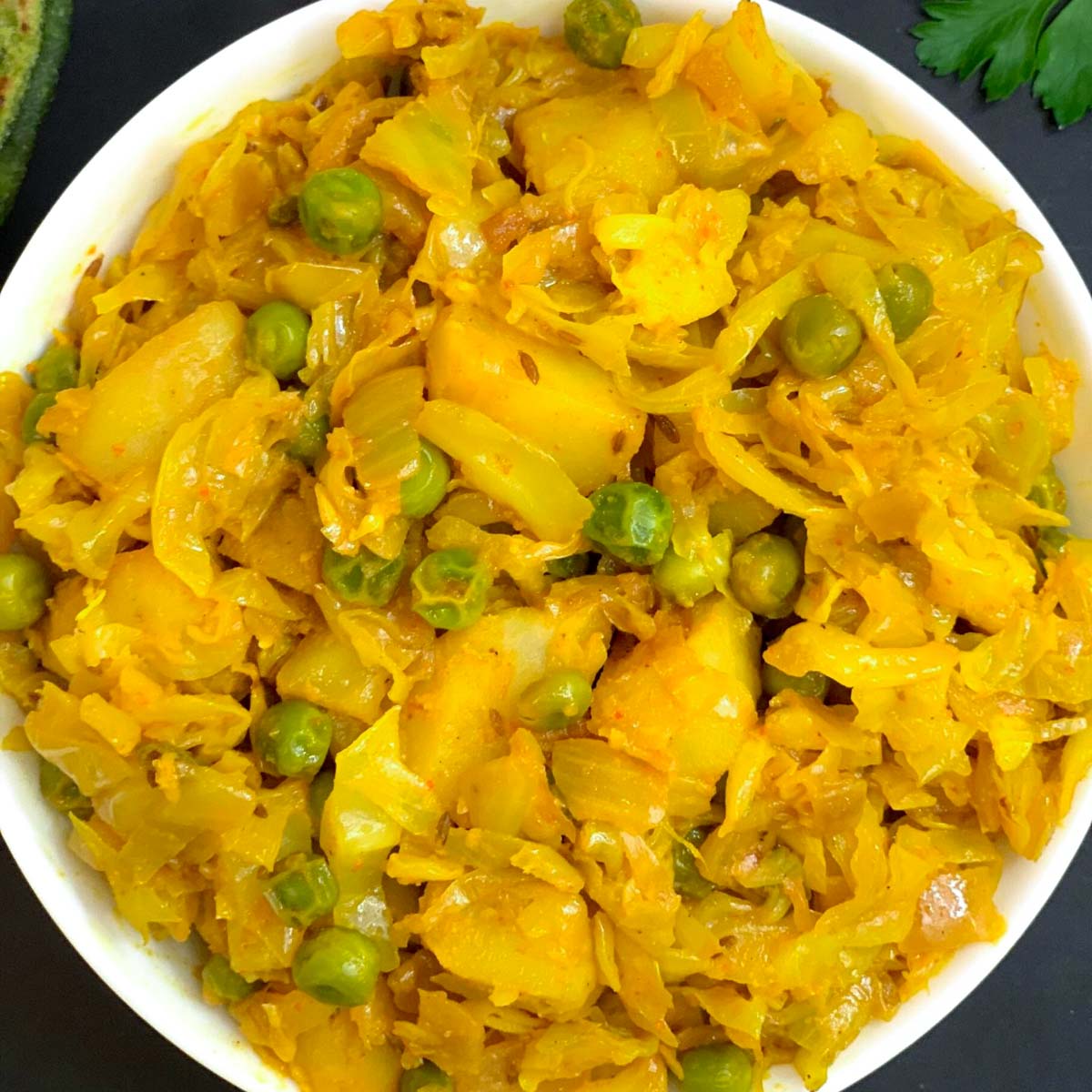 cabbage potato curry served in a white bowl with cilantro and paratha on side