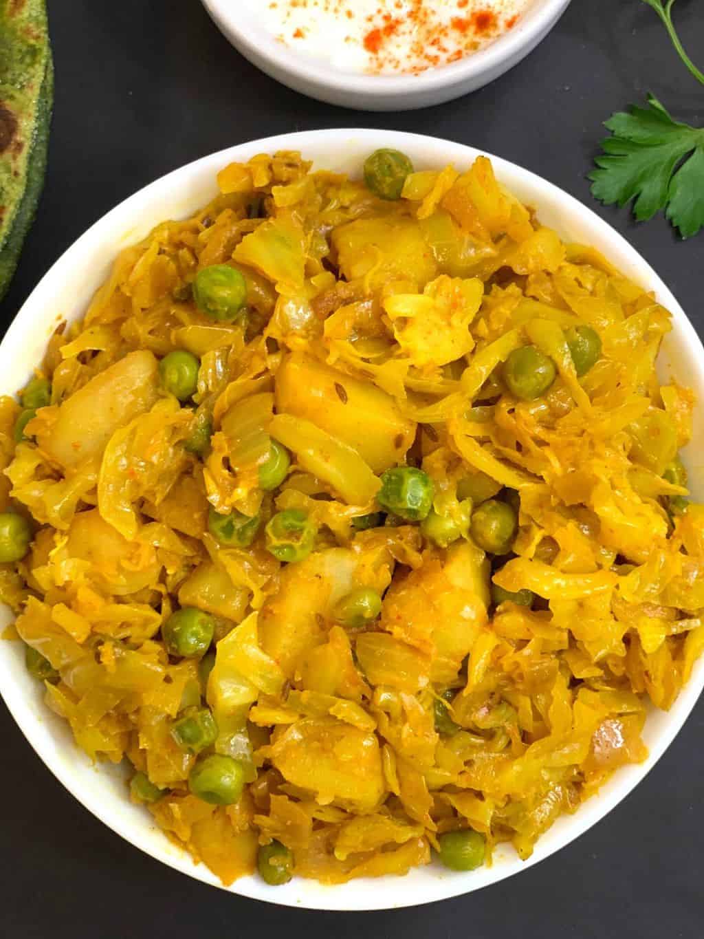 cabbage potato peas curry served in a bowl with raita on the side