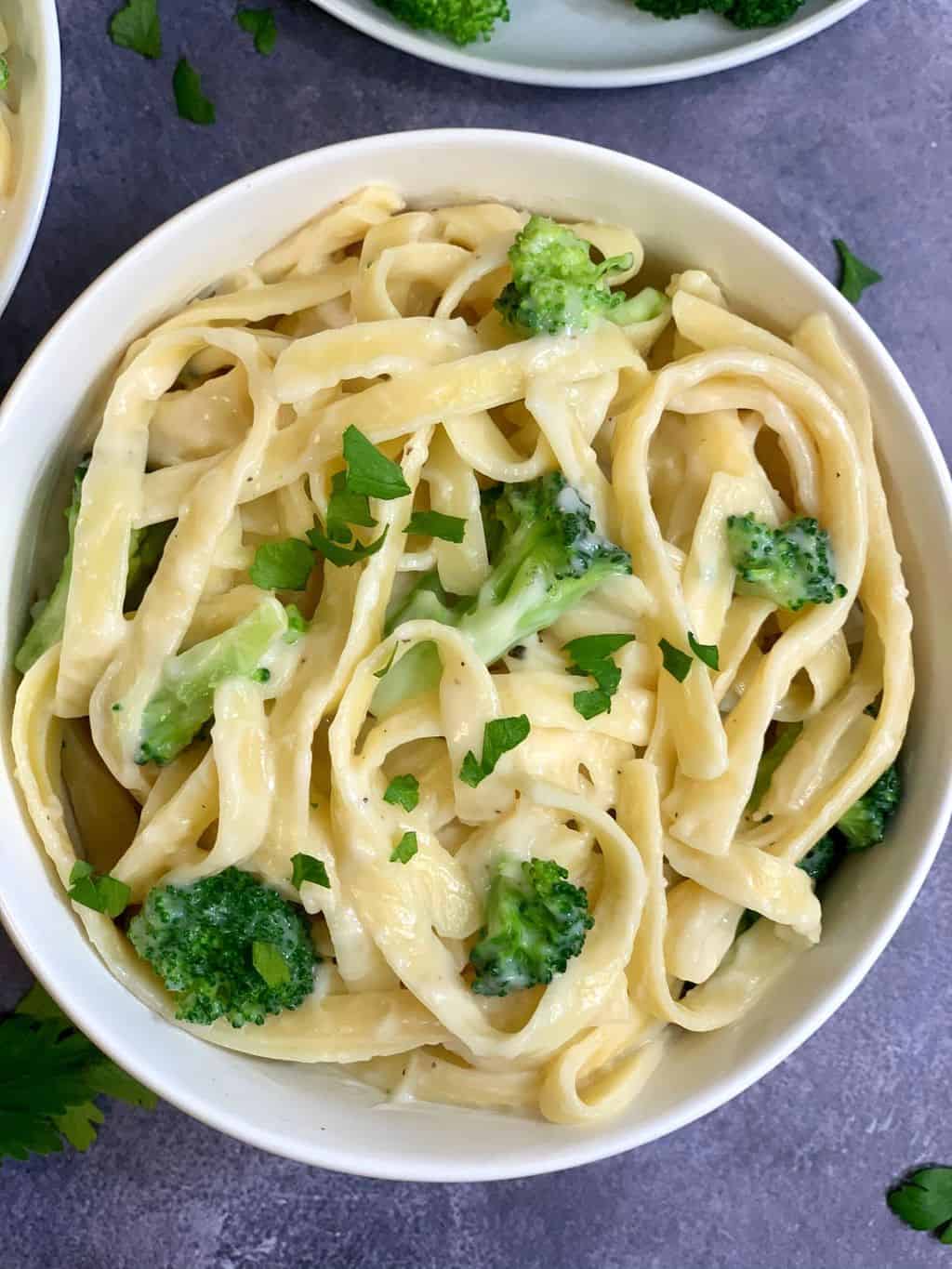 Fettucchini Alfredo served in a bowl garnished with steamed broccoli and parsley